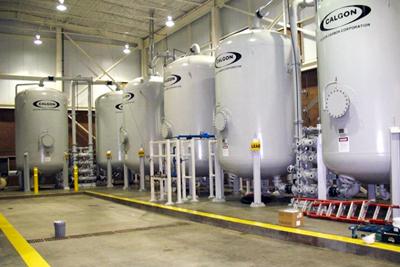 Six large white tanks labelled Calgon stand in a metal building with concrete floors.