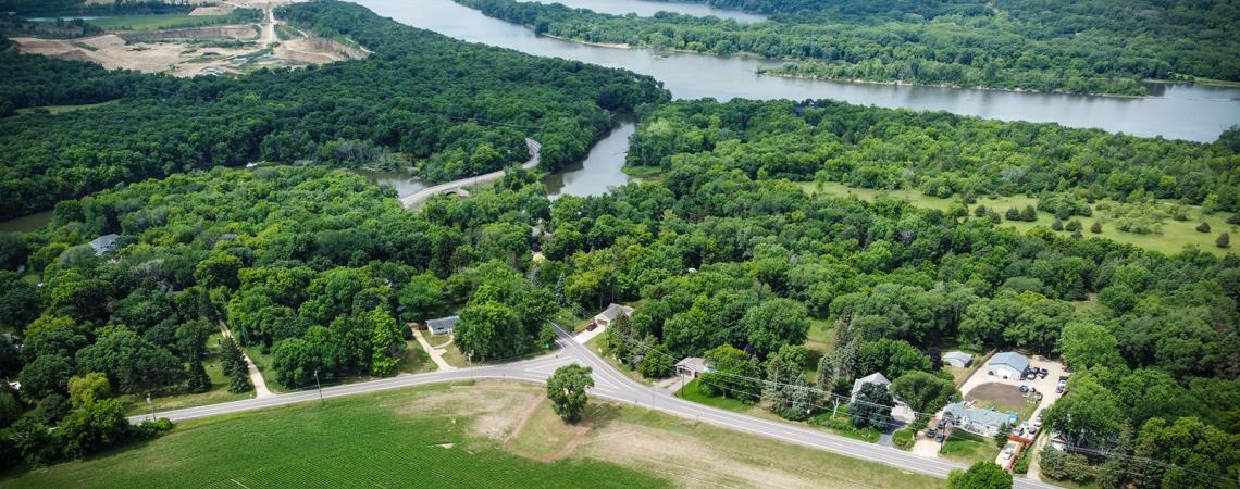 Aerial view of a road running along the edge of a wooded area next to a river.