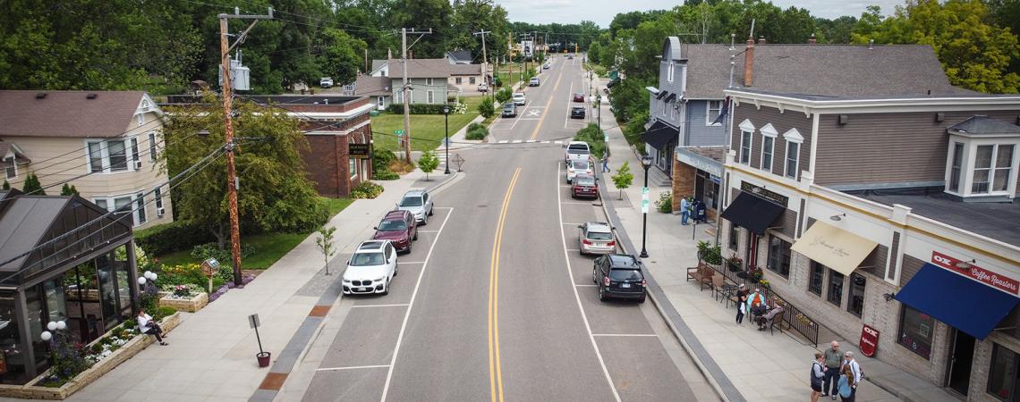 Aerial view of a road running through a small town with businesses and homes on each side of the road and people visiting on the sidewalk.