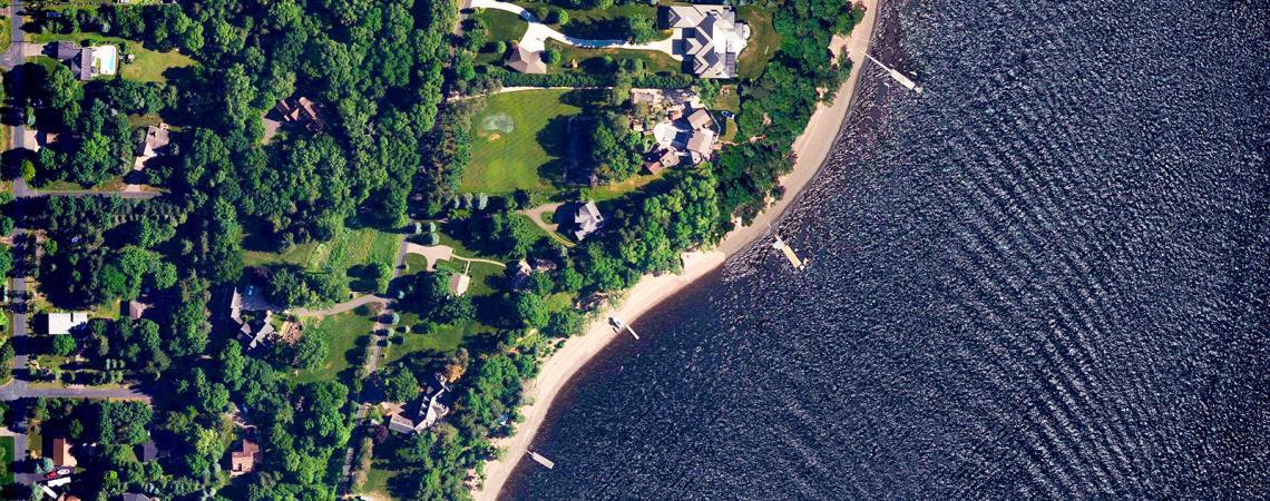 Bird's eye view of a wind rippled river and a tree-lined neighborhood next to it.