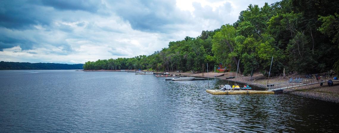 Tree-lined river bank with docks along the shoreline.