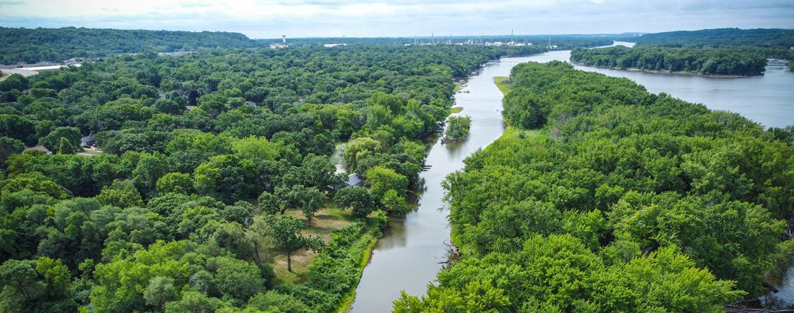 Aerial view of a river running through trees, with a small tree-covered island in the distance.