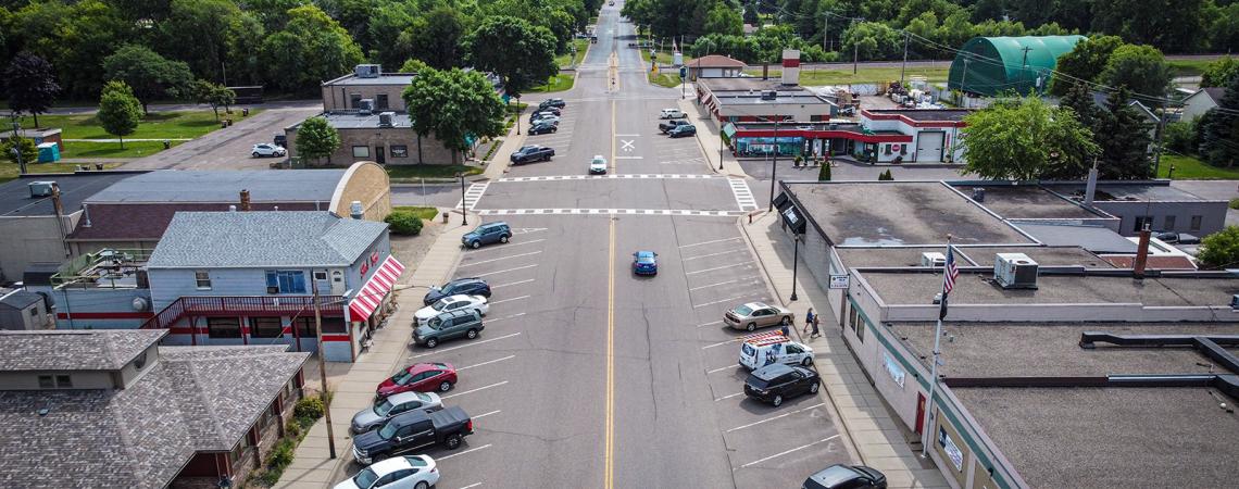 Aerial view of a road running through a small town. Businesses are on each side of the road with cars parked in front of them.