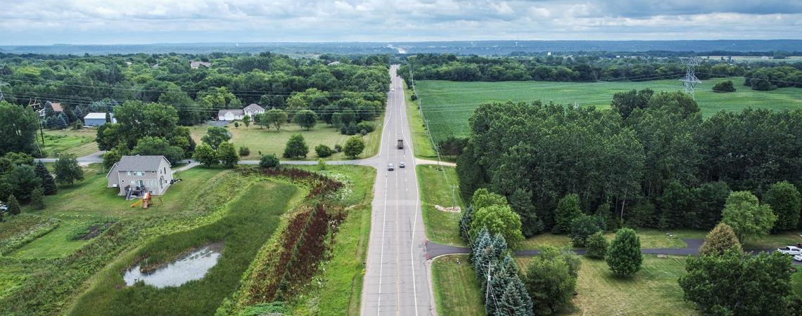 Aerial view of a highway running through a rural area of trees, fields, and homes.